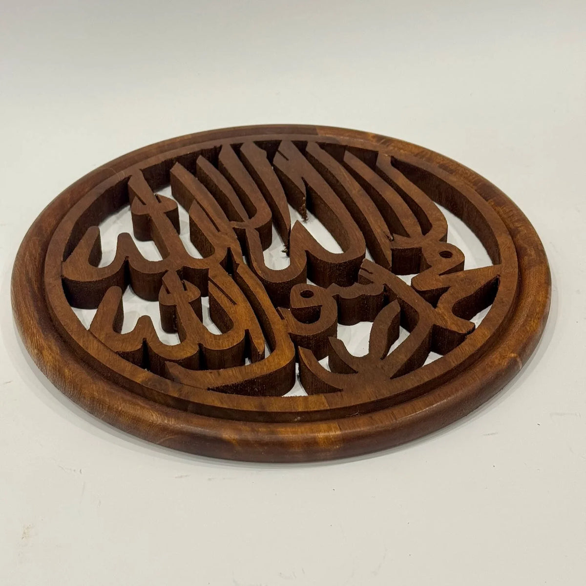 Hand carved wooden Kalma calligraphy wall art in a round frame, openwork lettering, front view