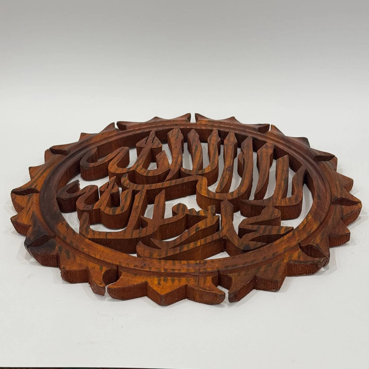 Round wooden Allahu Akbar calligraphy wall hanging at an angle, showing the carved openwork letters