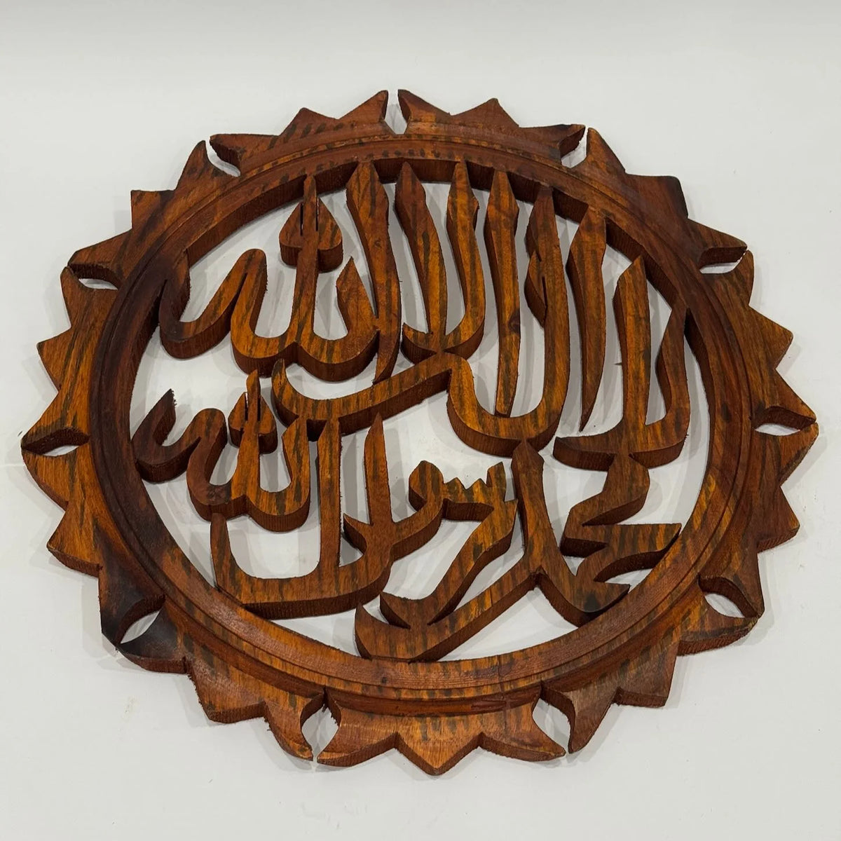 Large 14 inch hand carved wooden Kalma calligraphy wall art with a sunburst scalloped border in a warm reddish finish