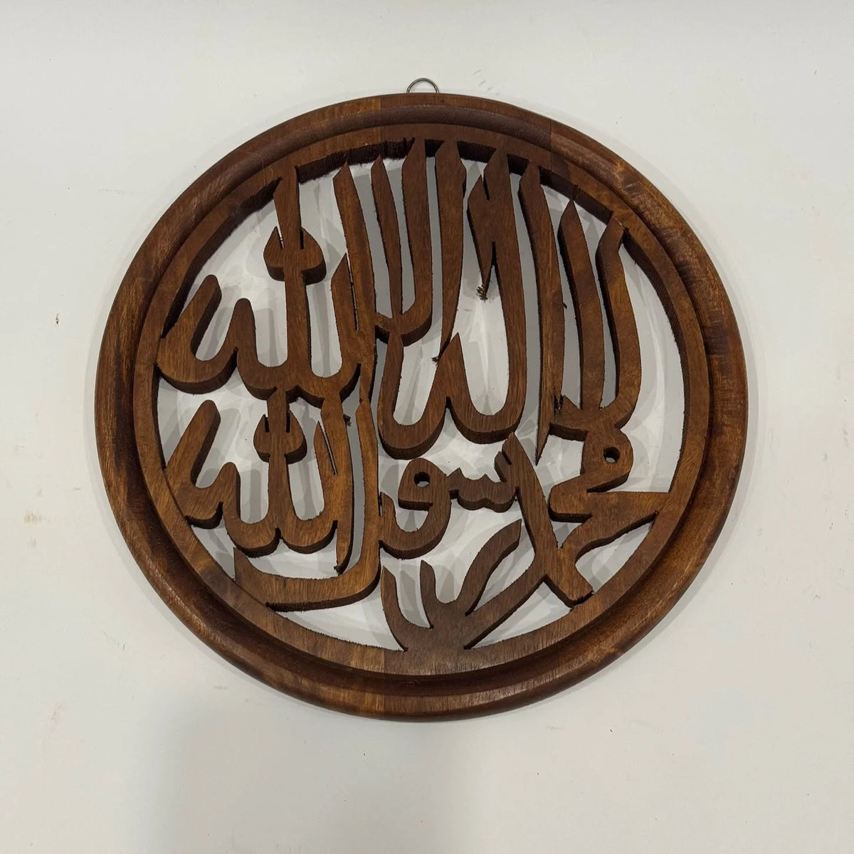 Round wooden Kalma calligraphy wall hanging at an angle, showing the depth of the cut-through lettering