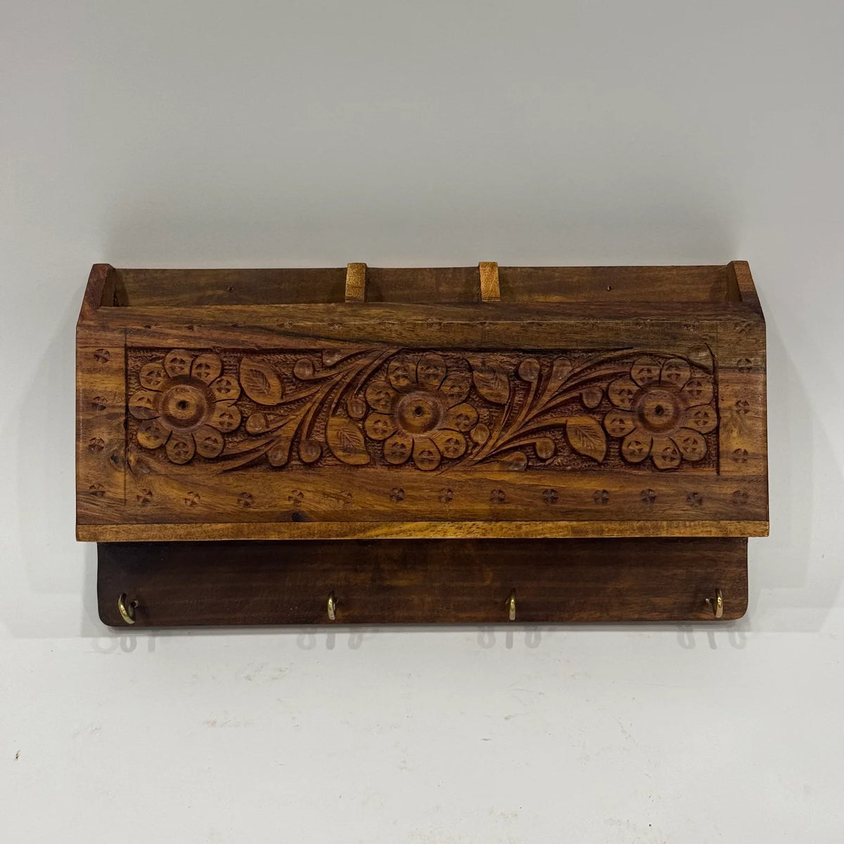 Front view of hand carved wooden mobile and key holder with floral carving, three compartments and brass key hooks