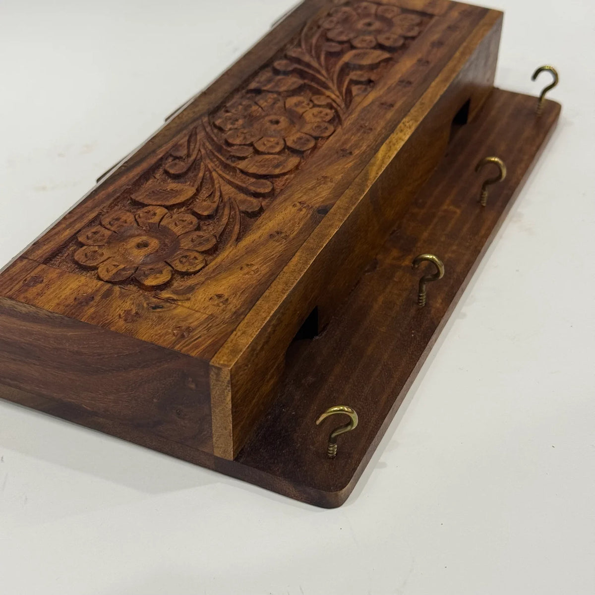 Side angle of carved wooden key holder organizer showing the floral carving and brass screw-in key hooks